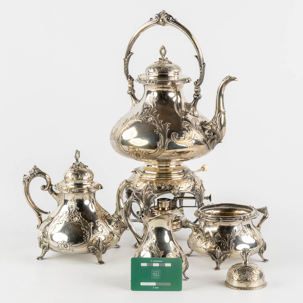 Een verzilverd koffie en theeservies met samovar, suikerpot, melkkan en tafelbel. H&Co. (L:20 x W:26 x H:44 cm)