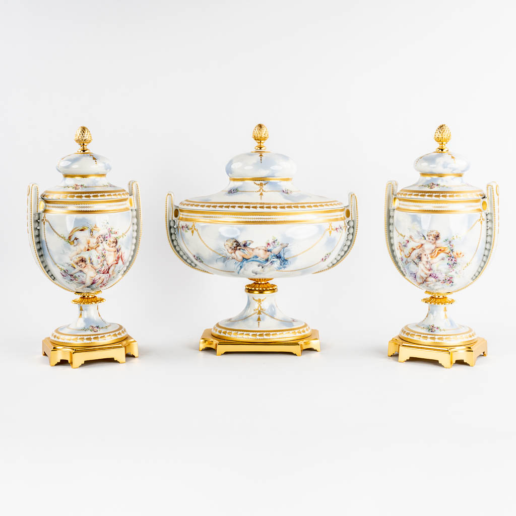 A three piece mantle garniture, porcelain vases with a lid, decorated with Angels. Italy, 20th C.