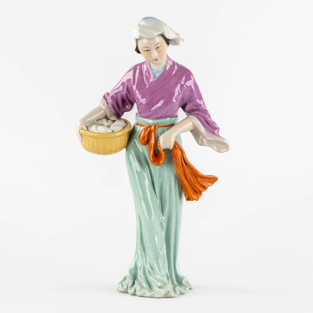 Een Chinees porseleinen figuur van een dame met mand. (L:11 x W:18 x H:32,5 cm)