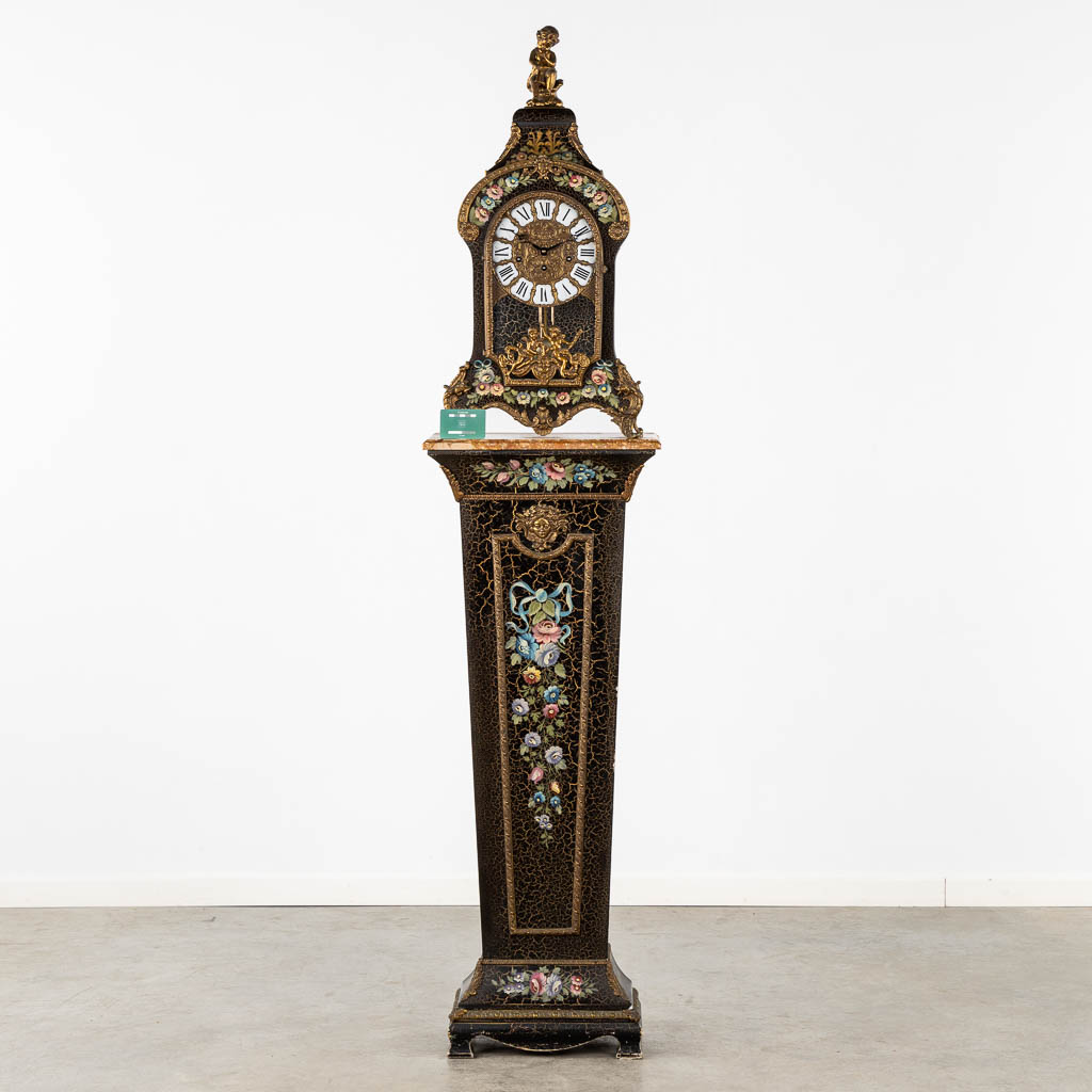 A cartel clock on a base, floral decor and mounted with putti. 20th C. (L:25 x W:44 x H:193 cm)