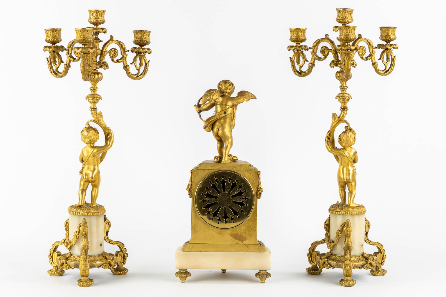 A three-piece mantle garniture clock, Cupid. Gilt bronze and Carrara marble. (L:13 x W:17 x H:37 cm)