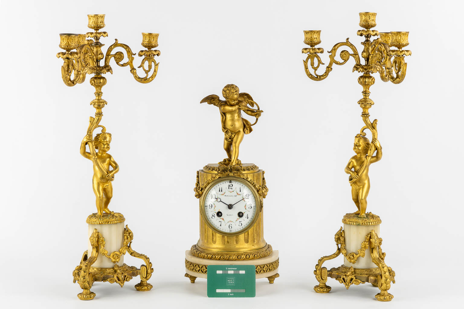 A three-piece mantle garniture clock, Cupid. Gilt bronze and Carrara marble. (L:13 x W:17 x H:37 cm)