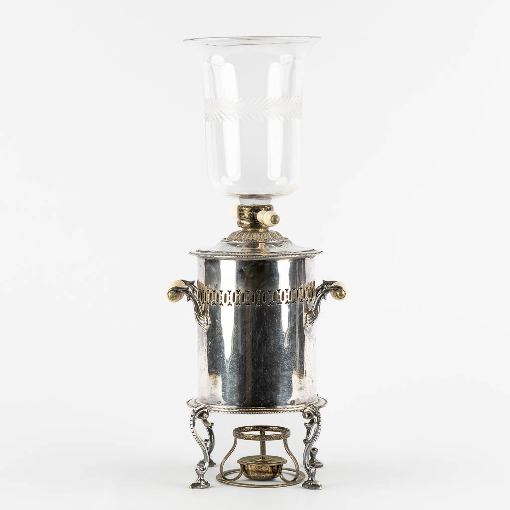 Een verzilverde samovar met glas, staande op leeuwen. (W:33 x H:51 cm)