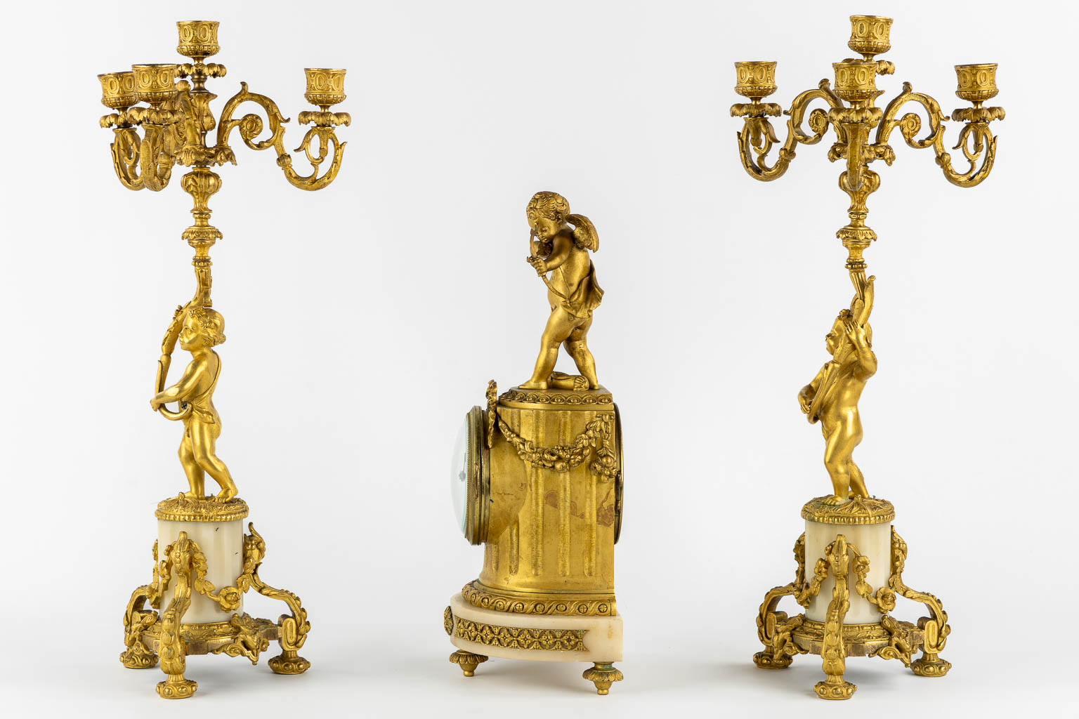 A three-piece mantle garniture clock, Cupid. Gilt bronze and Carrara marble. (L:13 x W:17 x H:37 cm)