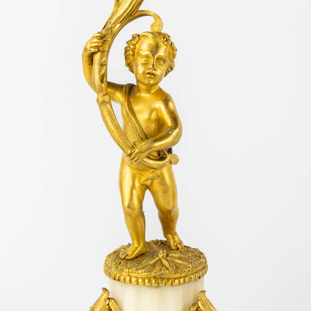 A three-piece mantle garniture clock, Cupid. Gilt bronze and Carrara marble. (L:13 x W:17 x H:37 cm)