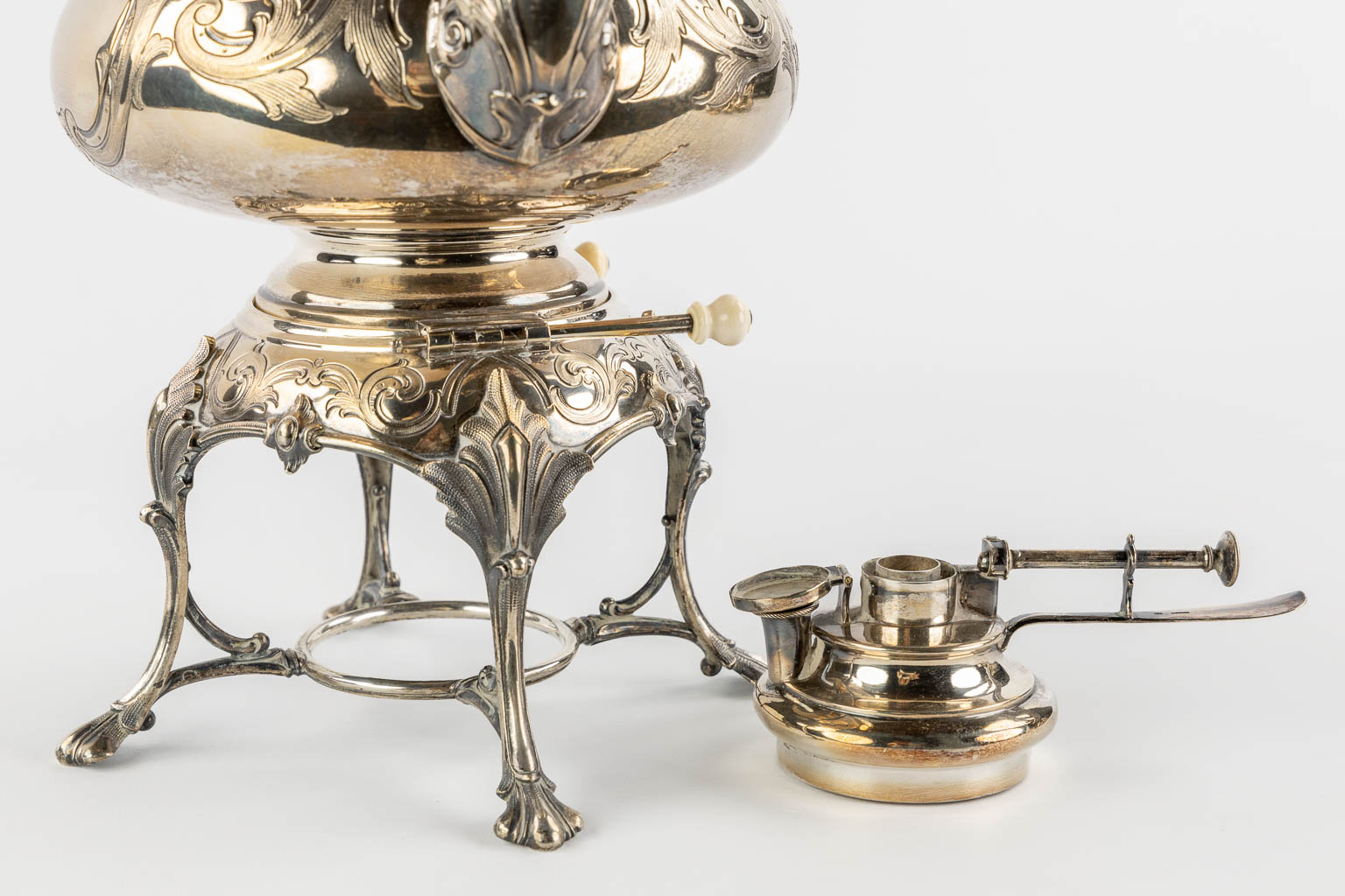 Een verzilverd koffie en theeservies met samovar, suikerpot, melkkan en tafelbel. H&Co. (L:20 x W:26 x H:44 cm)