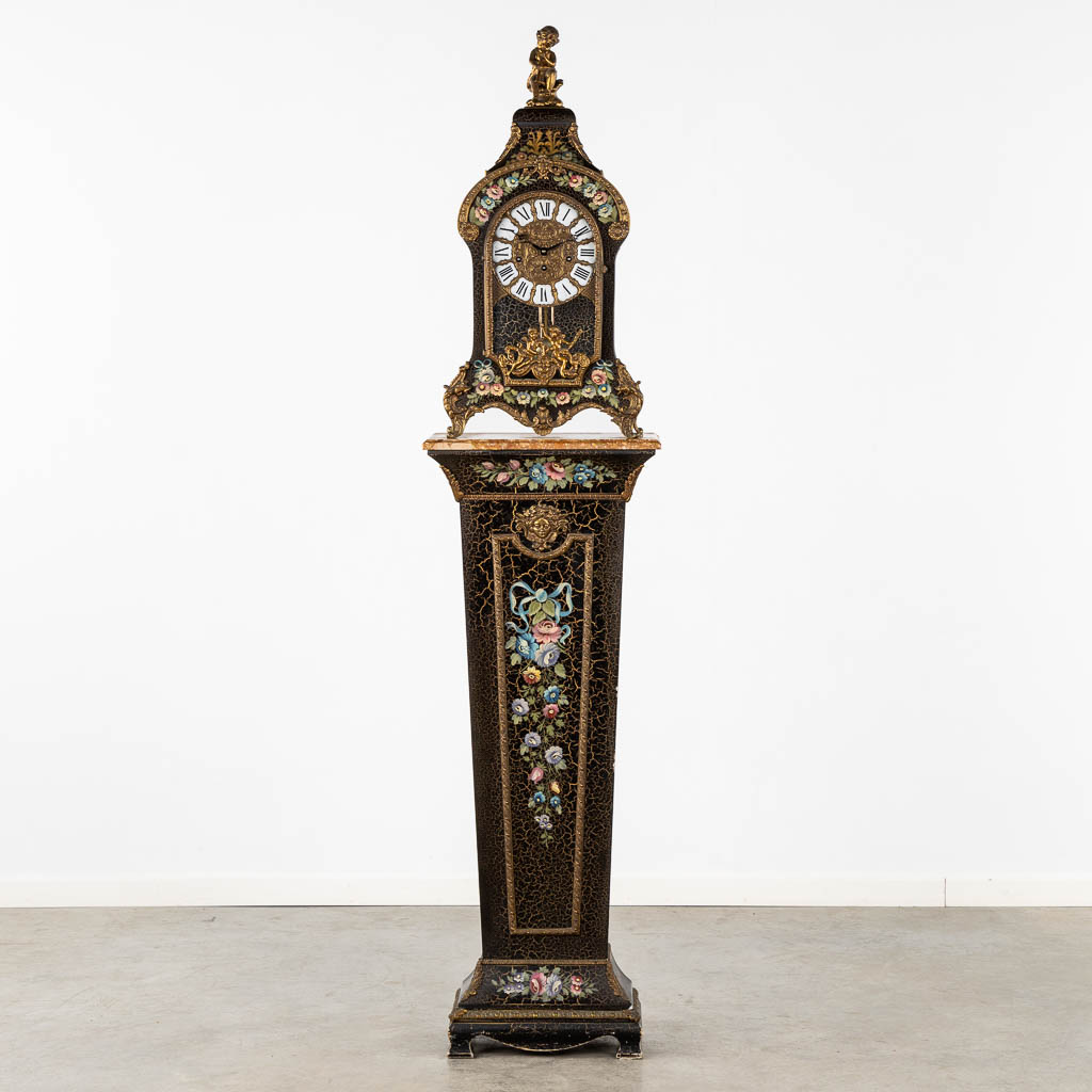 A cartel clock on a base, floral decor and mounted with putti. 20th C. (L:25 x W:44 x H:193 cm)