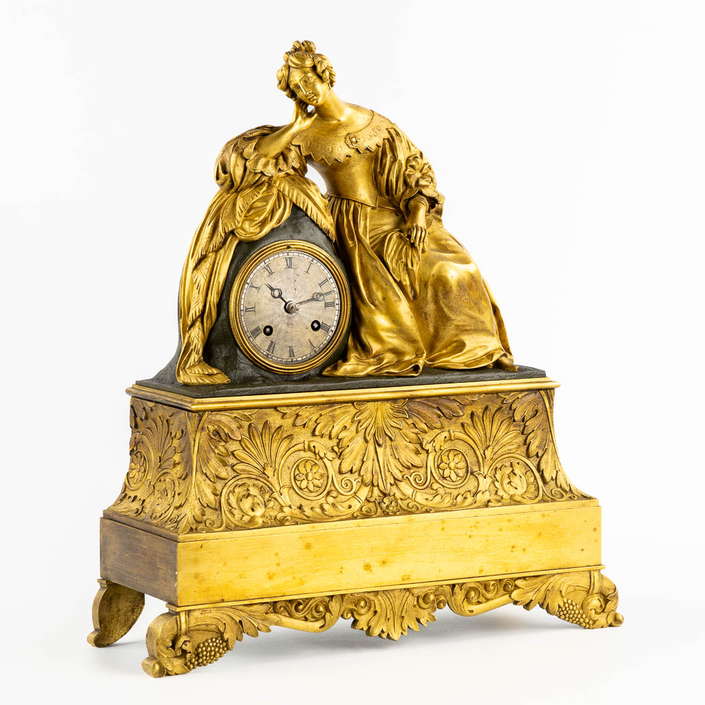 A mantle clock with a resting lady, gilt bronze. France, 19th C. (L:13 x W:38 x H:43 cm)