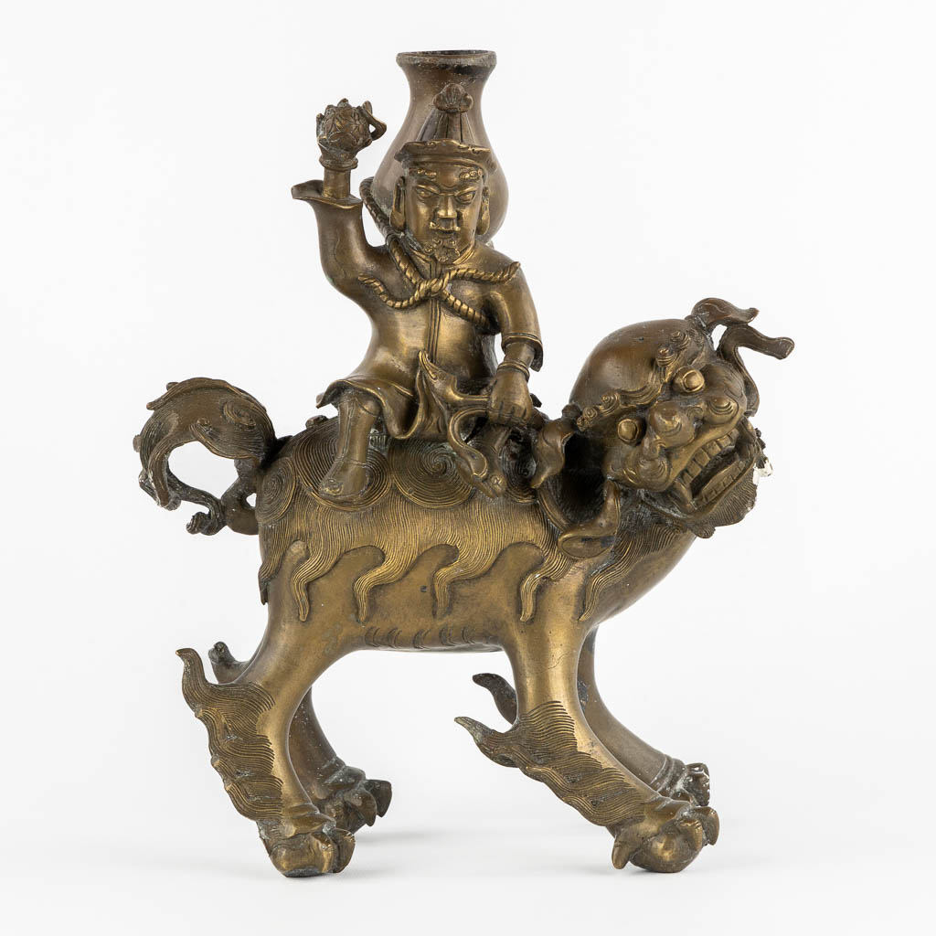 A decorative Asian figurine of a man riding a Foo Dog. Patinated bronze.