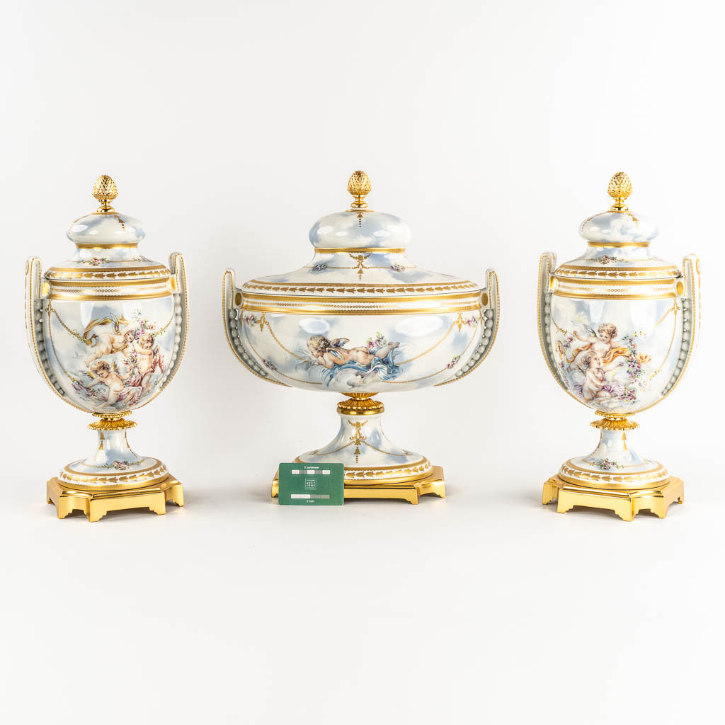 A three piece mantle garniture, porcelain vases with a lid, decorated with Angels. Italy, 20th C.