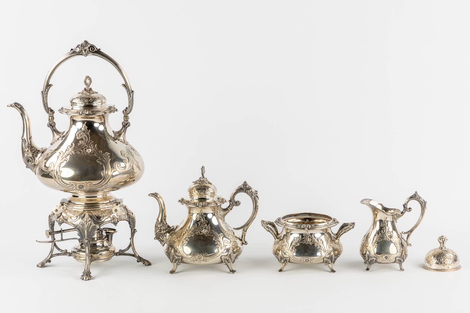 Een verzilverd koffie en theeservies met samovar, suikerpot, melkkan en tafelbel. H&Co. (L:20 x W:26 x H:44 cm)