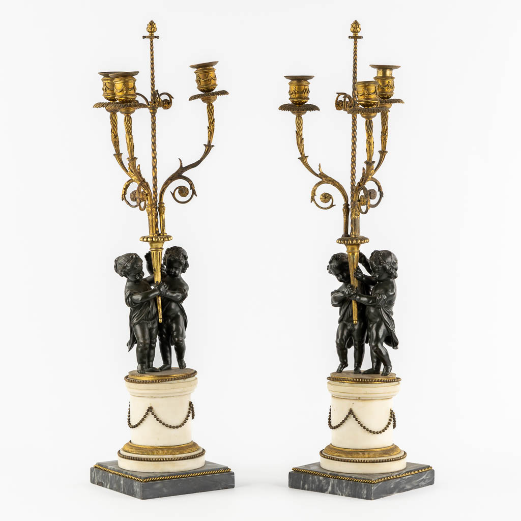  Een paar marmer, verguld en gepatineerd bronzen kandelaars met putti, Lodewijk XVI stijl, 19de eeuw.