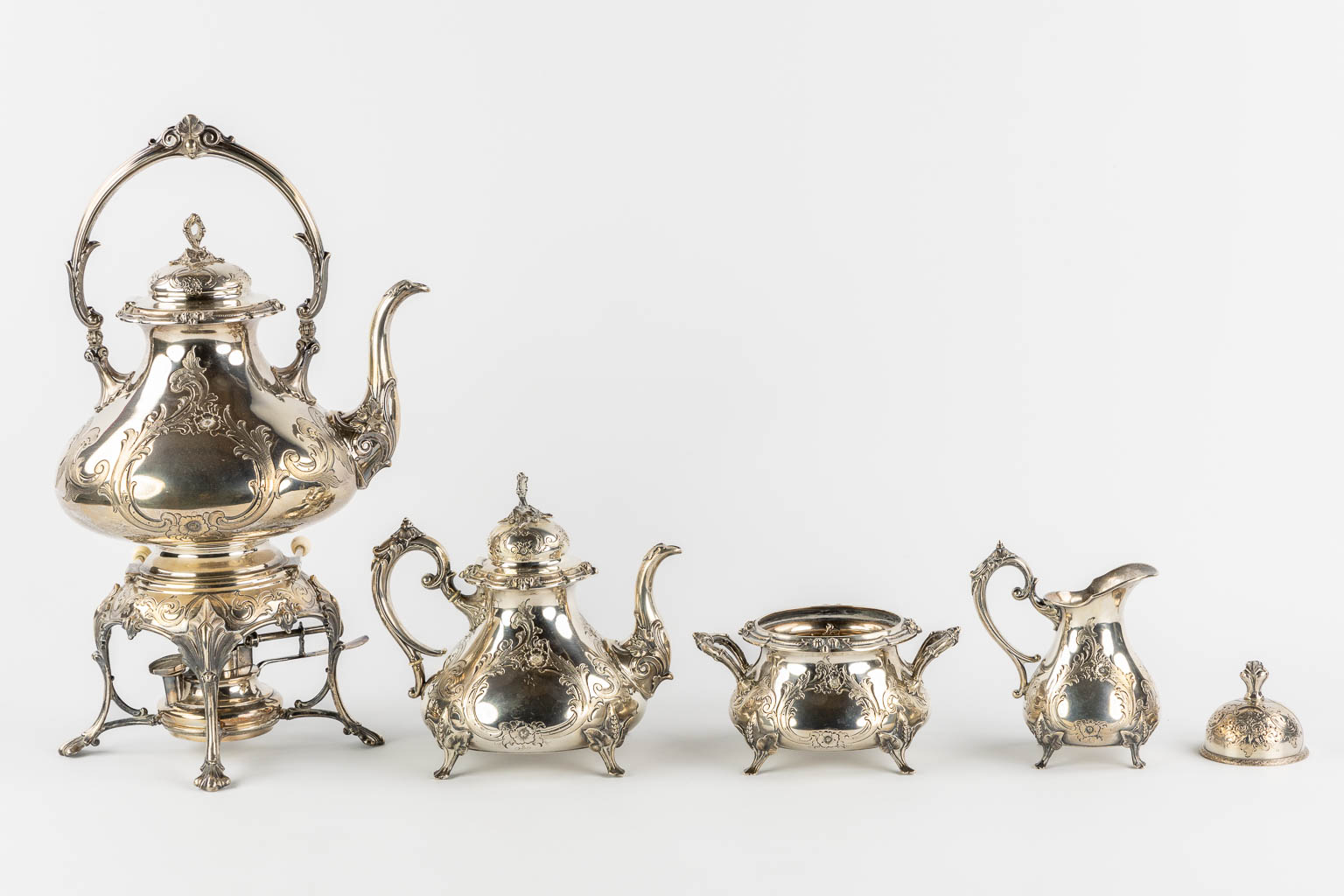 Een verzilverd koffie en theeservies met samovar, suikerpot, melkkan en tafelbel. H&Co. (L:20 x W:26 x H:44 cm)