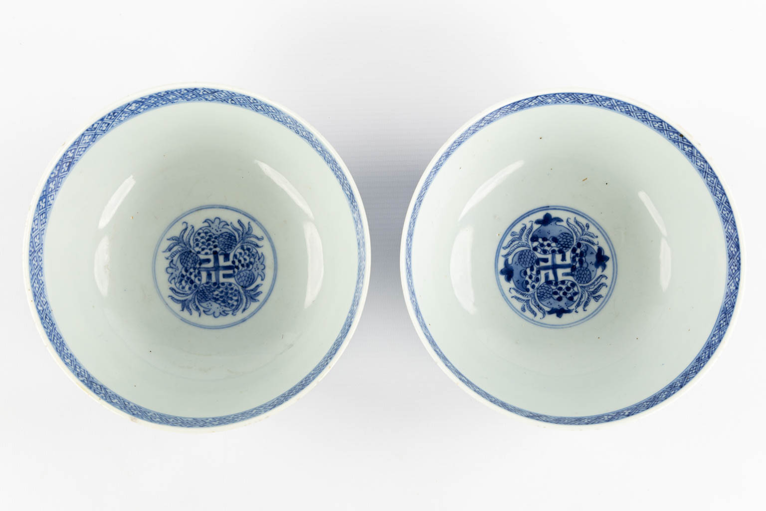 A pair of Chinese bowls, blue-white with a floral and pomegranate decor. 19th C. (H:8,5 x D:18 cm)