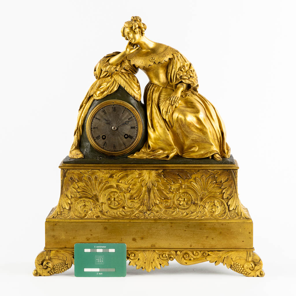 A mantle clock with a resting lady, gilt bronze. France, 19th C. (L:13 x W:38 x H:43 cm)