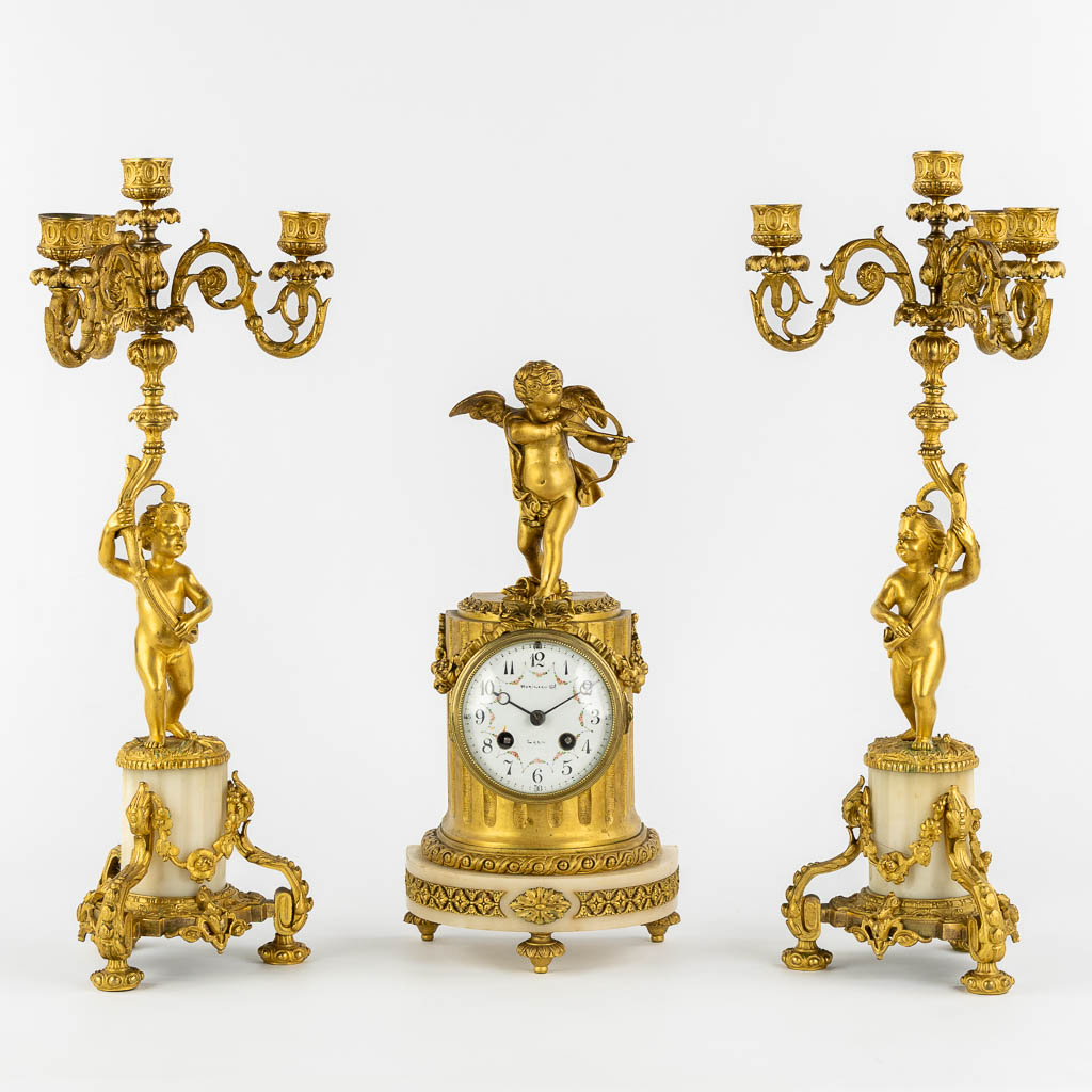 A three-piece mantle garniture clock, Cupid. Gilt bronze and Carrara marble. (L:13 x W:17 x H:37 cm)