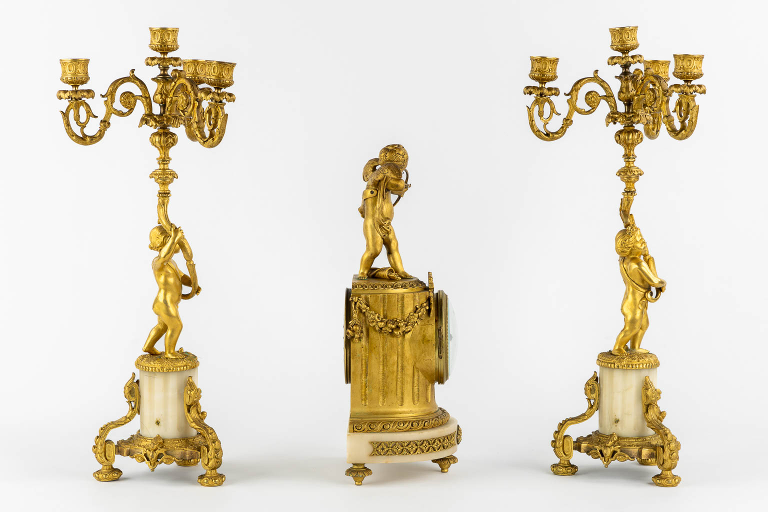 A three-piece mantle garniture clock, Cupid. Gilt bronze and Carrara marble. (L:13 x W:17 x H:37 cm)