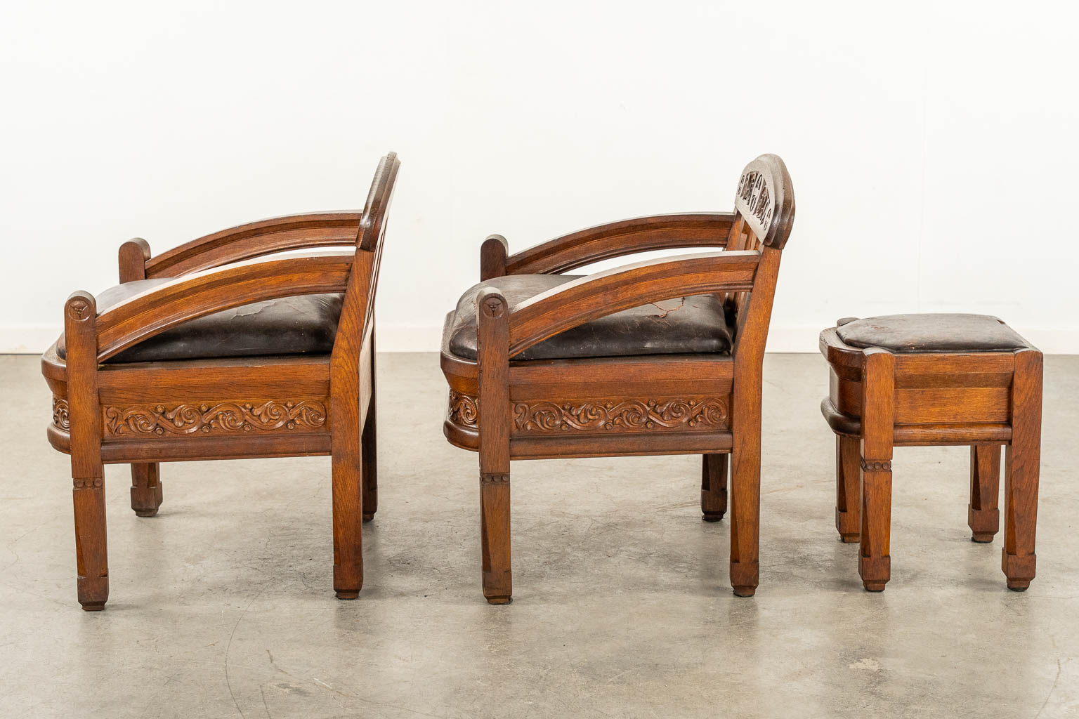 A pair of sculptured wood armchairs and footstool, used in an Art Deco chapel, leather seat. (L:60 x W:60 x H:73 cm)